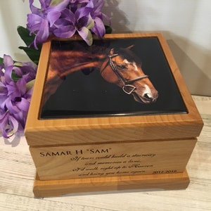 May include: A wooden memorial box with a photo of a brown horse's head on the lid. The box has engraved text that reads "SAMAR H 'SAM'" and a poem. Purple flowers are in the background.