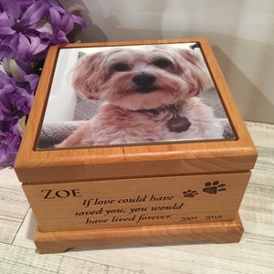 May include: A wooden pet memorial box with a photo of a dog on the lid. The box has engraved text that reads "ZOE" and "If love could have saved you, you would have lived forever. 2009-2018." Paw prints are also engraved on the box.