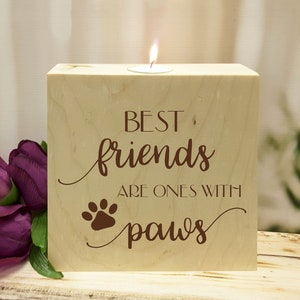 May include: Wooden candle holder with the text "Best friends are ones with paws" and a paw print. The candle holder is light brown and has a small tea light candle in the center.