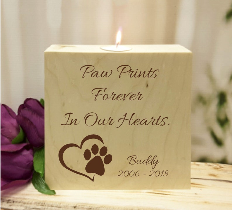 May include: Wooden candle holder with the text "Paw Prints Forever In Our Hearts."  A brown paw print is inside a heart shape. The text "Buddy 2006-2018" is below the heart.