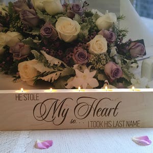 May include: A wooden candle holder with four candle slots. The holder is engraved with the text "He stole my heart so... I took his last name".