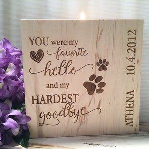 May include: A wooden memorial candle with the text "YOU were my favorite hello and my HARDEST goodbye" and two paw prints. The candle is engraved with the name "ATHENA" and the date "10.4.2012".