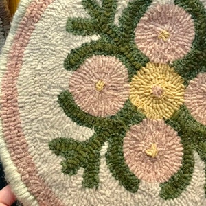 May include: A round, cream-coloured rug with a floral design. The rug features pink, yellow, and green flowers with a white background.