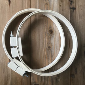 May include: Two wooden embroidery hoops, one nested inside the other, on a wooden surface. The hoops are made of natural wood and have a smooth finish.