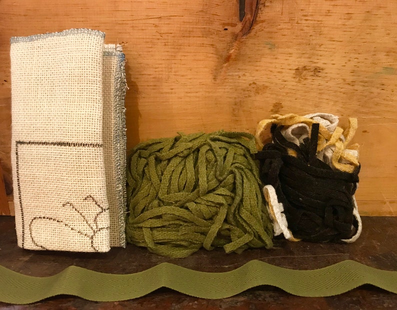 K&ouml;nnte beinhalten: Ein Set an Stickzubeh&ouml;r, bestehend aus einem St&uuml;ck wei&szlig;en Leinenstoff mit einer braunen Umrandung einer Blume, einem B&uuml;ndel gr&uuml;nem Garn und einem B&uuml;ndel schwarzem, wei&szlig;em und gelbem Garn.