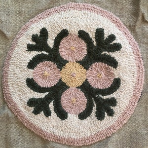 May include: A round, cream-coloured rug with a pink and green floral design. The rug has a circular pattern of four pink and yellow circles with a green leafy design around them.