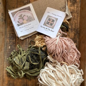 May include: A rug hooking kit with instructions and wool yarn in pink, green, and white. The kit includes a pattern for a floral design with the text "The Bee & The Bear" and "001 - Vintage Flowers".