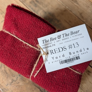 May include: A bundle of red fabric tied with twine, with a tag that reads "REDS #13 Yard Bundle." The tag also includes the text "The Bee & The Bear" and "Handmade Dry Goods Vintage."