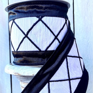 May include: A roll of decorative ribbon with a white background and a black diamond pattern. The ribbon has black edges and is displayed on a white pedestal. The text "RITZY GLITZY WREATHS" is visible.