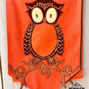 May include: Orange felt table runner with a brown owl applique decorated with gold sequins. The owl is perched on a brown branch. The table runner has a brown border and the text "Ritzy Glitzy Wreaths" is printed in the bottom right corner.