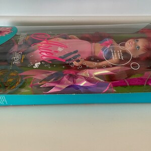 Pode incluir: Uma boneca Ariel rosa e azul do filme da Disney A Pequena Sereia. A boneca est&aacute; usando uma cauda de sereia rosa e azul e tem cabelo comprido e vermelho. A caixa apresenta o texto "Cool Tween Ariel Teenager" e "Disney's The Little Mermaid Sirene Supreme".