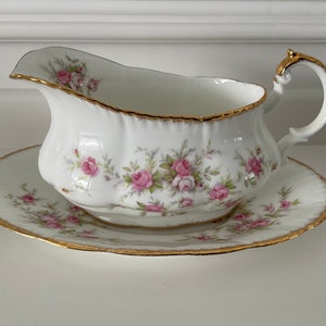 Peut inclure: Un saucier en porcelaine blanche avec une bordure dorée et un motif de roses roses. Le saucier est sur une soucoupe assortie.