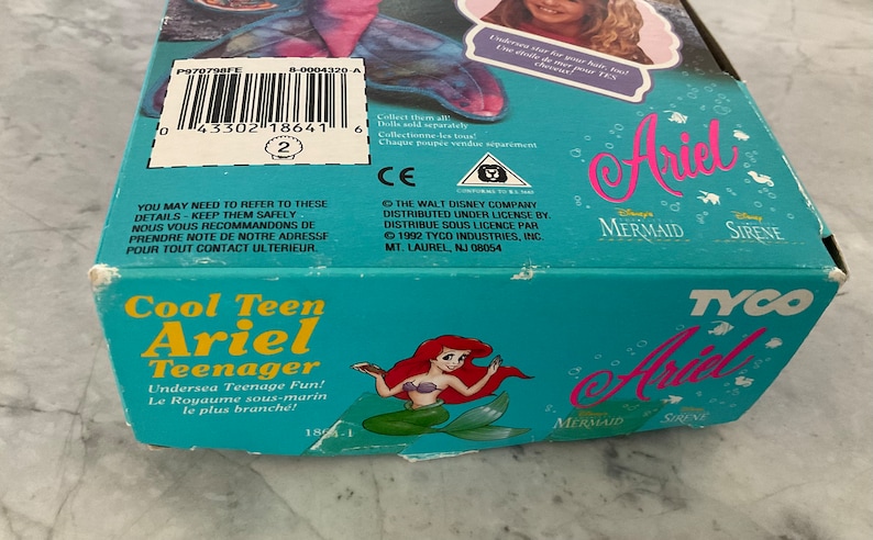 Pode incluir: Uma caixa azul e verde com uma imagem de Ariel de A Pequena Sereia na frente. A caixa diz "Cool Teen Ariel Teenager" e "Undersea Teenage Fun!" A caixa &eacute; para uma boneca ou um brinquedo.