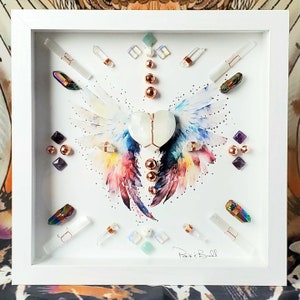 May include: A white framed artwork featuring a watercolor painting of colorful wings with a white heart in the center. The artwork is decorated with various crystals, beads, and metallic accents. The signature "Paris & Bull" is visible in the bottom right corner.