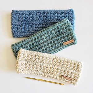 May include: Three crocheted headbands in different colours: blue, teal, and cream. Each headband has a small brown leather tag with the text "Love & Stitch". A gold crochet hook is also pictured.