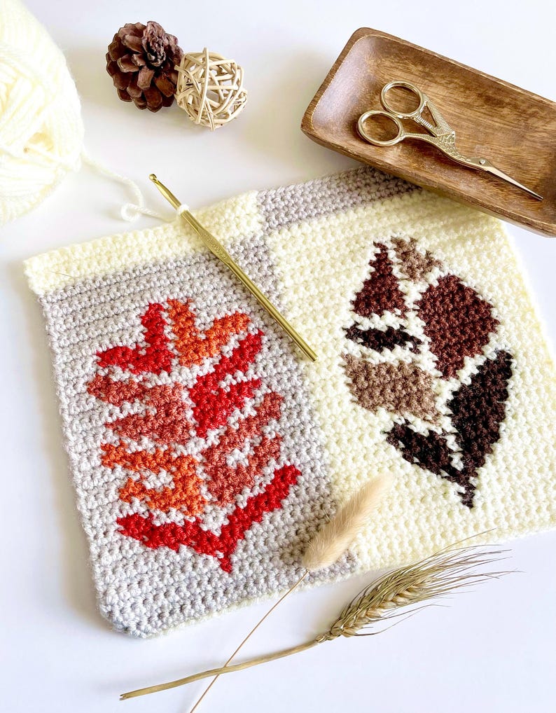 May include: A close-up of a handmade crochet project featuring two leaf designs. One leaf is red and orange, the other is brown and beige. A gold crochet hook, scissors, and yarn are also visible.