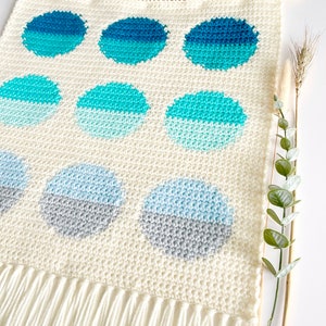 May include: A white crocheted wall hanging with a fringe border. The hanging features a pattern of blue and gray circles.