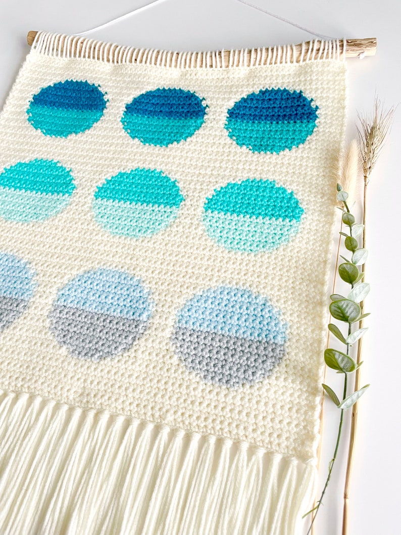 May include: A white crocheted wall hanging with a fringe border. The hanging features a pattern of blue and gray circles.