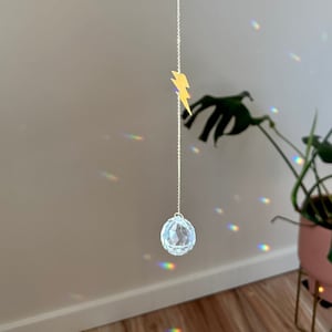 May include: A crystal ball hanging from a gold chain with a gold lightning bolt charm. The crystal ball is casting rainbows on the wall.