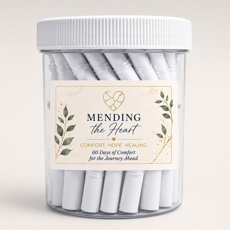 May include: A clear plastic jar with a white ribbed lid, filled with tightly rolled white paper scrolls. The label features a gold cracked heart icon, green leaf illustrations, and the text MENDING the Heart COMFORT HOPE HEALING 60 Days of Comfort for the Journey Ahead.