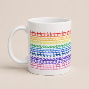 Può includere: Una tazza in ceramica bianca caratterizzata da una serie di fasce orizzontali con un gradiente di colori dell'arcobaleno. Ogni fascia presenta un motivo decorativo a linee ripetitive unico, inclusi vortici, onde e forme geometriche in rosso, arancione, giallo, verde, blu, indaco, viola e rosa.