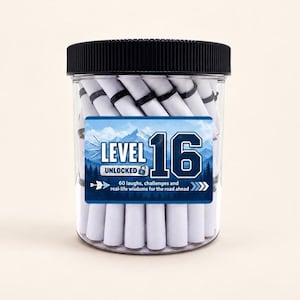 Può includere: Un barattolo di plastica trasparente con coperchio nero a coste riempito di rotoli di carta bianchi legati con fascette nere. L'etichetta presenta una grafica di montagna blu, il testo "LEVEL 16 UNLOCKED" e "60 laughs, challenges and real-life wisdoms for the road ahead."