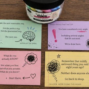 May include: A clear plastic jar with a black lid sits above four rectangular cards in light green, purple, pink, and yellow. Each card features printed text and black ink illustrations including a brain, an exclamation point, a heart, and scribbles.