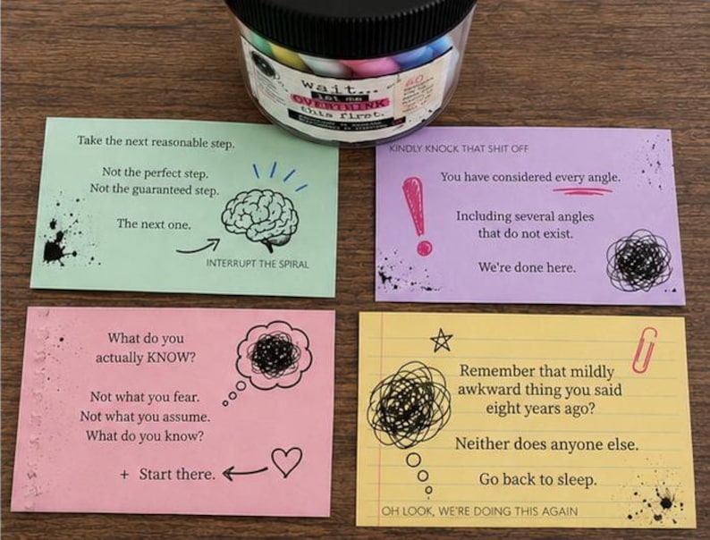 May include: A clear plastic jar with a black lid sits above four rectangular cards in light green, purple, pink, and yellow. Each card features printed text and black ink illustrations including a brain, an exclamation point, a heart, and scribbles.