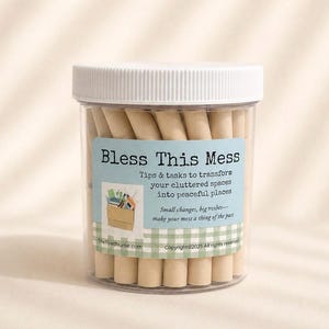 May include: A clear plastic jar with a white screw-top lid containing rolled beige paper slips. The label features the text Bless This Mess, Tips & tasks to transform your cluttered spaces into peaceful places, and a graphic of a cardboard box.