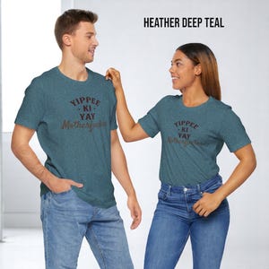 May include: Two people wearing matching heather deep teal t-shirts with the text "Yippee-Ki-Yay Motherf*cker" printed in brown. The man is wearing blue jeans and the woman is wearing blue jeans.