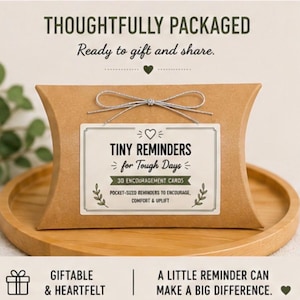 May include: A brown cardboard pillow box tied with a silver string. A white label on the front reads: THOUGHTFULLY PACKAGED, Ready to gift and share, TINY REMINDERS for Tough Days, 30 ENCOURAGEMENT CARDS, POCKET-SIZED REMINDERS TO ENCOURAGE, COMFORT & UPLIFT.