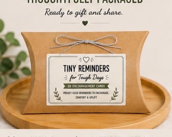May include: A brown cardboard pillow box tied with a silver string, featuring a white label that reads: THOUGHTFULLY PACKAGED, TINY REMINDERS for Tough Days, 30 ENCOURAGEMENT CARDS, POCKET-SIZED REMINDERS TO ENCOURAGE, COMFORT & UPLIFT.