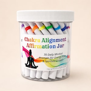 May include: A clear plastic jar with a white lid containing rolled white paper scrolls secured with colorful rubber bands. The label reads Chakra Alignment Affirmation Jar, 70 Daily Mindset Prompts for Energy Flow & Spiritual Growth.