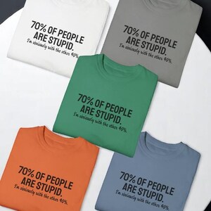 May include: Five crew neck t-shirts in white, gray, green, orange, and blue. Each shirt features the black printed text: 70% OF PEOPLE ARE STUPID. I'm obviously with the other 40%. The shirts are arranged in a circular pattern on a white surface.