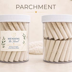 May include: Two clear plastic jars with white lids filled with rolled parchment paper scrolls. The left jar features a label with the text MENDING the Heart, COMFORT HOPE HEALING, and 60 Days of Comfort for the Journey Ahead, decorated with green leaves.