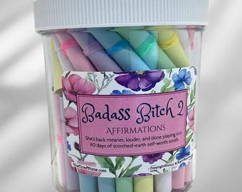 May include: A clear plastic jar with a white lid filled with colorful scrolls. The jar has a label that reads "Badass Bitch 2 AFFIRMATIONS" with text about self-worth. The scrolls are various pastel colors.