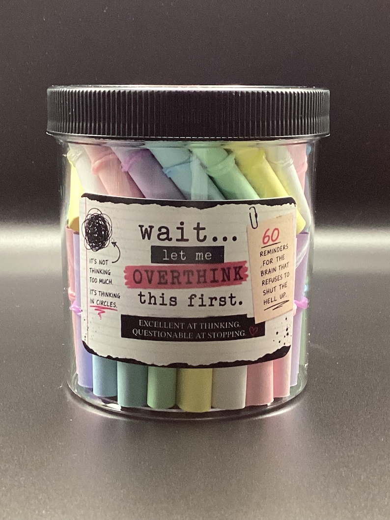 May include: A clear plastic jar with a black lid filled with pastel-colored paper rolls. The label reads: wait... let me OVERTHINK this first. It includes text: 60 REMINDERS FOR THE BRAIN THAT REFUSES TO SHUT THE HELL UP and EXCELLENT AT THINKING, QUESTIONABLE AT STOPPING.