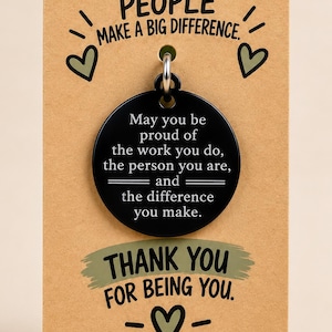 May include: A round black metal keychain pendant engraved with the text: May you be proud of the work you do, the person you are, and the difference you make. It is attached to a tan card printed with Good People Make A Big Difference and Thank You.