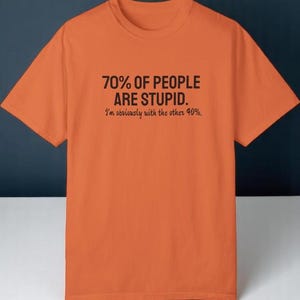 May include: An orange short-sleeved t-shirt featuring black text printed on the chest that reads: 70% OF PEOPLE ARE STUPID. I'm obviously with the other 40%. The shirt has a crew neckline and a standard fit, constructed from a solid-colored fabric.