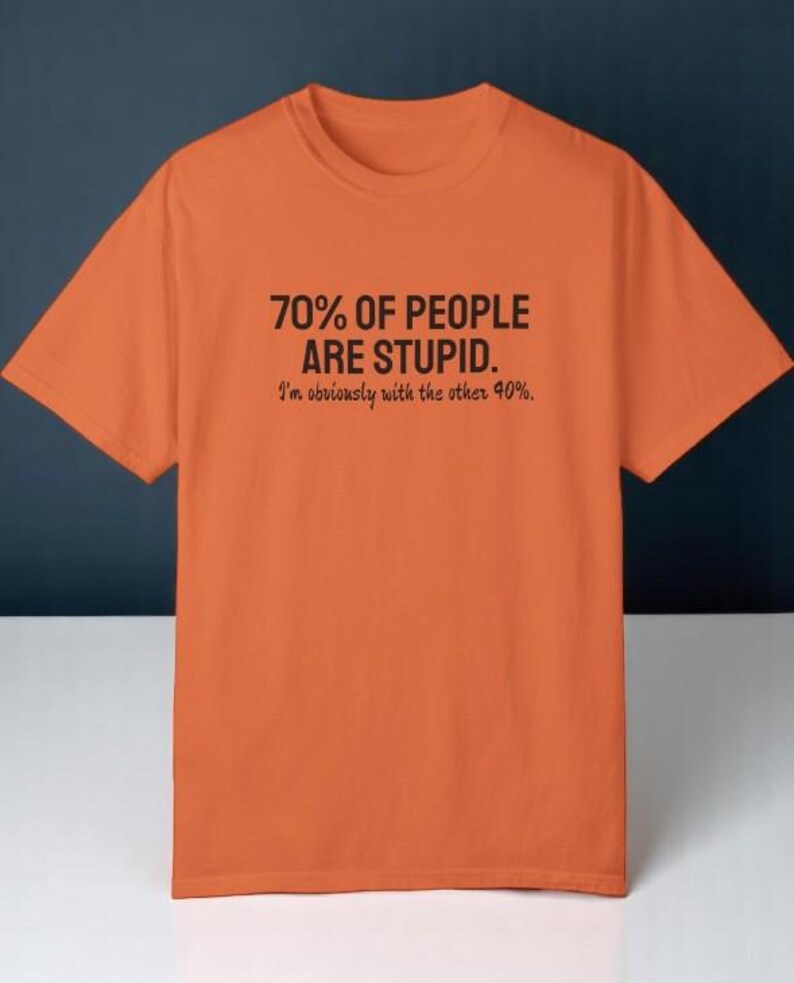 May include: An orange short-sleeved t-shirt featuring black text printed on the chest that reads: 70% OF PEOPLE ARE STUPID. I'm obviously with the other 40%. The shirt has a crew neckline and a standard fit, constructed from a solid-colored fabric.