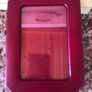 May include: A red leather picture frame with a textured surface. The frame has a clear glass insert and is designed to hold a photograph.