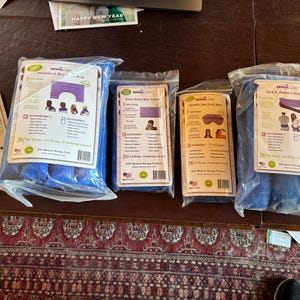 May include: An assortment of blue SensaCare natural therapy packs in clear plastic packaging. The packs include a shoulder wrap, a back and abdomen wrap, and two face relief wraps. Each pack has a white label with product information and illustrations.