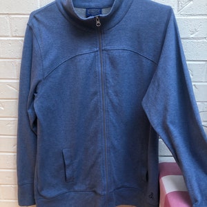 May include: A blue zip-up jacket with a high collar and a small pocket on the front. The jacket has a full zipper and the brand name "Pendleton" is visible on the collar. The jacket is hanging on a gray hanger.