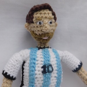May include: Crocheted doll wearing a blue and white striped jersey with the number 10 on the front. The doll has brown hair, a beard, and a friendly expression.