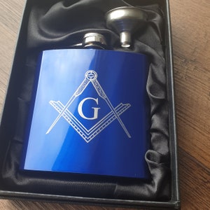 Könnte beinhalten: Eine blaue Edelstahl-Taschenflasche mit einem silbernen freimaurerischen Symbol, das auf die Vorderseite graviert ist. Die Flasche befindet sich in einer schwarzen Samtbox mit einem silbernen Trichter.