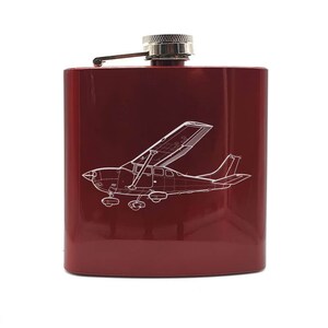 May include: A red metal flask with a silver cap and a white outline of a small airplane engraved on the front.