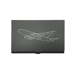 May include: A black business card holder with a white outline of a passenger airplane. The airplane design is detailed, showing the wings, engines, and fuselage. The card holder is rectangular and has a small clasp.