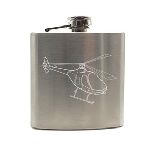May include: A stainless steel hip flask with a brushed metal finish. A white outline of a helicopter is etched on the front. The flask has a hinged cap and a small spout. The flask is designed to hold liquids.