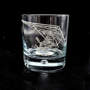 May include: A clear, lowball glass with a detailed etched design of a hang glider. The hang glider illustration is white and covers a large portion of the glass. The glass has a rounded base and a thick bottom.