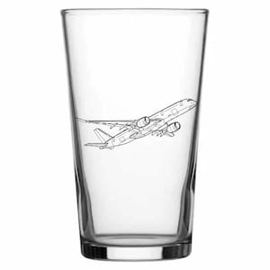May include: A clear pint glass featuring a black outline of a passenger aeroplane in flight. The glass has a cylindrical shape with a flared top and a solid base. The aeroplane illustration is detailed.